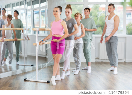 Teacher conducts class with teen girls and boys in ballet studio, observes doing Batman exercise. 114479294