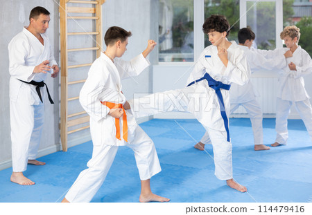 Twen boys in kimonos honing karate kicking techniques during kumite Twen boys in kimonos honing karate kicking techniques during kumite 114479416