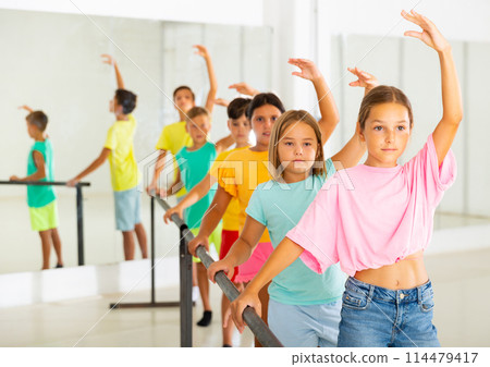 Focused tween girl practicing ballet positions near bar during group class 114479417