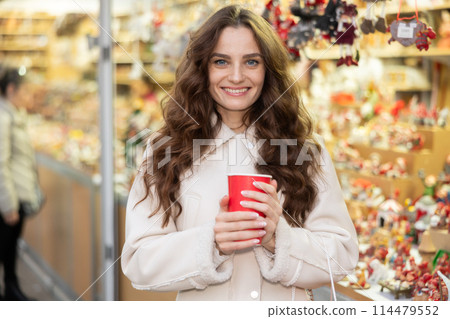 Cheerful woman with paper cup of hot tea walking at Christmas street fair 114479552
