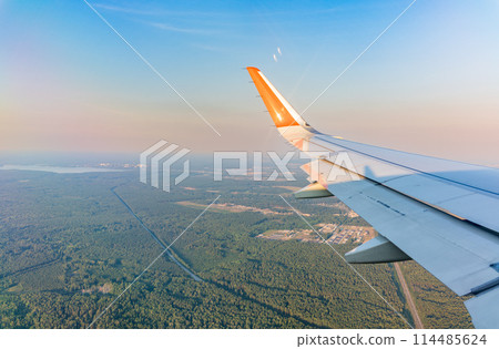 View of airplane wing, blue skies and green land during landing. Airplane window view. 114485624