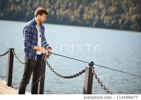 Fisherman standing on riverside and trying to catch fish Fisherman standing on riverside and trying to catch fish 114486677