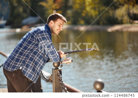young fisherman with rod and sunglasses fishing in lake young fisherman with rod and sunglasses fishing in lake 114486745