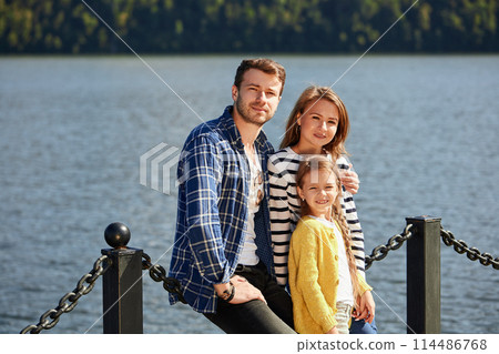 Happy Family looking at camera while posing on pier at quiet lake 114486768