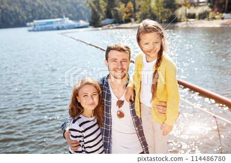 Happy Family looking at camera while posing on pier at quiet lake 114486780