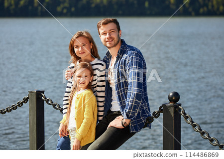 Happy Family looking at camera while posing on pier at quiet lake 114486869