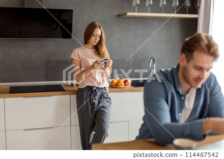 cunny woman is checking her husband's phone while he working at the laptop cunny woman is checking her husband's phone while he working at the laptop 114487542