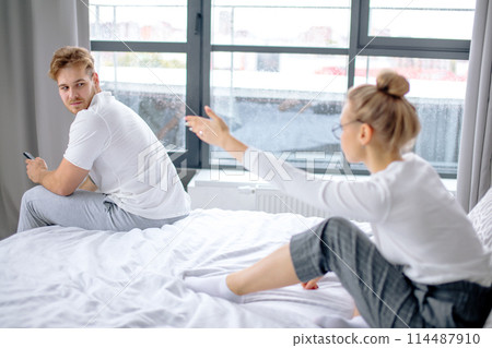 serious man is looking back while his wife is scolding him for laziness 114487910