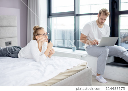 serious blond woman staring at TV while her boyfriend is sending e-mail 114488575