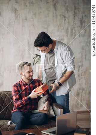 Happy surprised young handsome gay couple celebrating and giving gift at home 114489741