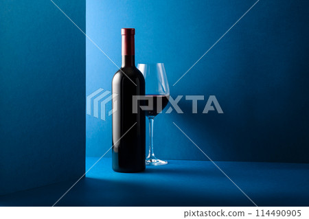 Bottle and glass of red wine on a blue background. 114490905