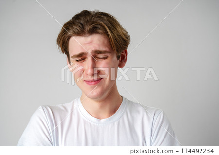 Young Man With Brown Hair Expressing Sadness Against a Plain Background Young Man With Brown Hair Expressing Sadness Against a Plain Background 114492234