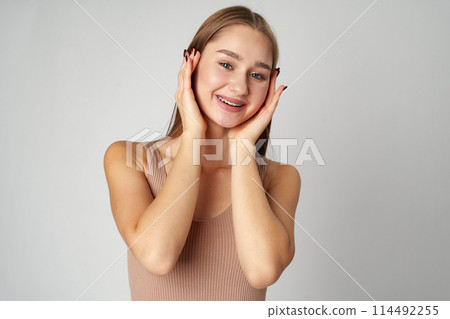 Woman Posing With Hands on Face against gray background Woman Posing With Hands on Face against gray background 114492255