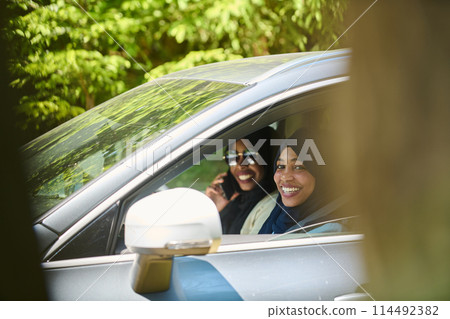 Two Muslim women wearing hijab converse on a smartphone while traveling together in a car through the  114492382