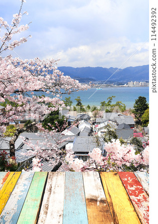 Blank wooden table top and aerial view on sea, houses and blooming sakura trees, Miyajima island, Japan. Traditional japanese hanami festival. Spring cherry blossoming season in Asia 114492392