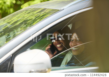 Two Muslim women wearing hijab converse on a smartphone while traveling together in a car through the  114492428