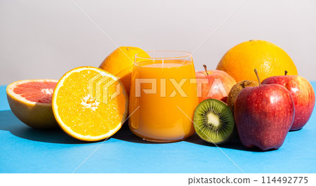 Multifruit juice in a glass among fresh fruits on blue and white background Multifruit juice in a glass among fresh fruits on blue and white background 114492775