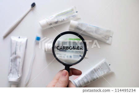 Dangerous toothpaste ingredient carbomer. Checking the composition of toothpaste with a magnifying glass against the background of many tubes Dangerous toothpaste ingredient carbomer. Checking the composition of toothpaste with a magnifying glass against the background of many tubes 114495234