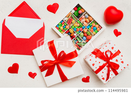 Red envelope with candy and gift box and Valentines hearts on colored background. Flat lay, top view. Romantic love letter for Holiday concept 114495981