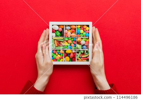 Female hands with delicious candies in box on color background 114496186
