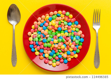 cutlery on table and sweet plate of candy. Health and obesity concept, top view on colored background cutlery on table and sweet plate of candy. Health and obesity concept, top view on colored background 114496385