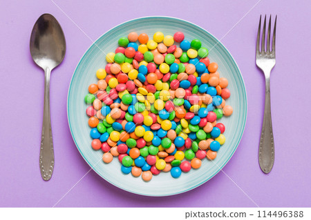 cutlery on table and sweet plate of candy. Health and obesity concept, top view on colored background cutlery on table and sweet plate of candy. Health and obesity concept, top view on colored background 114496388