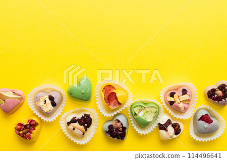 chocolate sweets in the form of a heart with fruits and nuts on a colored background. top view with space for text, holiday concept chocolate sweets in the form of a heart with fruits and nuts on a colored background. top view with space for text, holiday concept 114496641