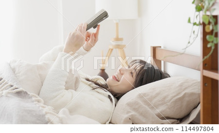 Asian woman looking at her smartphone after waking up Asian woman looking at her smartphone after waking up 114497804