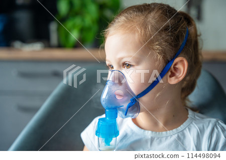 Cute little girl are sitting and holding a nebulizer mask leaning against the face, airway treatment concept 114498094