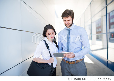 Businessman meeting with female coworker, going to business meeting in the city, holding tablet. Manager smiling, outdoor in urban setting 114498659