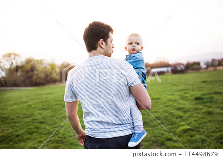 Portrait of father holding little toddler boy during warm spring day. Father's day concept. Portrait of father holding little toddler boy during warm spring day. Father's day concept. 114498679