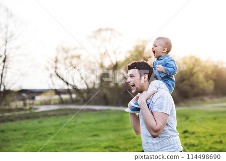 Father carrying little toddler on shoulders, having fun during warm spring day. Father's day concept. Father carrying little toddler on shoulders, having fun during warm spring day. Father's day concept. 114498690