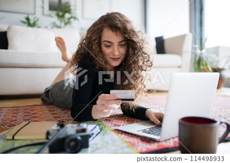 Beautiful woman planning summer vacation abroad, going on trip alone. Lying on floor, working on itinerary on laptop. Beautiful woman planning summer vacation abroad, going on trip alone. Lying on floor, working on itinerary on laptop. 114498933