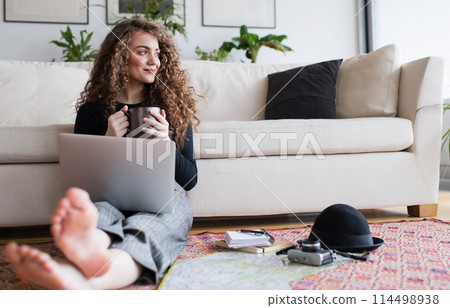 Beautiful woman planning summer vacation abroad, going on trip alone. Sitting on floor, working on itinerary on laptop. 114498938