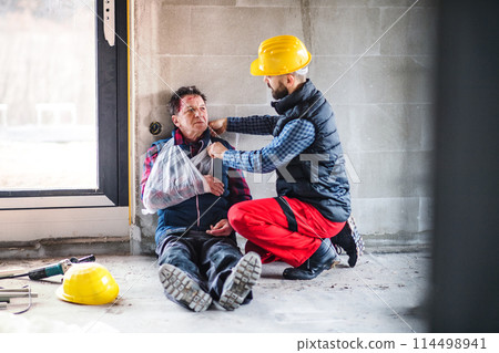 Colleague giving first aid to injured worker, in pain after accident at construction site Concept of occupational safety and health in workplace. 114498941