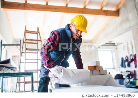 Older worker carrying heavy bag with building material. Work injury. 114498960