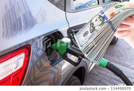 Gasoline pump gun to release fuel into passenger car and stack of american dollars Gasoline pump gun to release fuel into passenger car and stack of american dollars 114498970