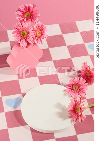 Photo was taken from above view at a table covered with pink checkered table cloth, decorated by some fresh pink gerbera daisy flower. Blank podium for presenting product has flower ingredient Photo was taken from above view at a table covered with pink checkered table cloth, decorated by some fresh pink gerbera daisy flower. Blank podium for presenting product has flower ingredient 114499006