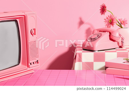 Pink concept photo with frontal shot, a television with pink color, a pink desk phone placed on the back table with a flower vase next to it. Vacant space on pink table for showing product 114499024