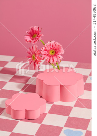 High angle shot at two pedestal in flower shaped displayed on pink checkered tablecloth with flor gerbera daisy decoration. Vertical photo for promotion with blank space for showing product 114499068