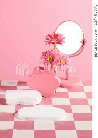 Vertical photo in pink and white tone, an empty tray placed in front, some pedestal, a mirror and gerbera flowers featured in back. Space for presentation, front view 114499076