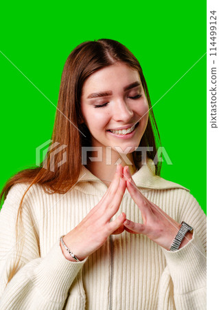 Young Woman Smiling With Closed Eyes on a Green Background Feeling Content 114499124