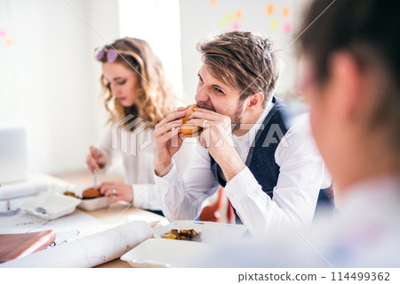 Young group of colleagues having quick lunch togeter in startup company office. Working in co-working space. 114499362