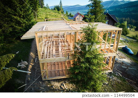 Bird's-eye view captured by drone showing two-level timber-framed dwelling in progress near a forest. The concept of contemporary ecological construction and modern architectural style. Bird's-eye view captured by drone showing two-level timber-framed dwelling in progress near a forest. The concept of contemporary ecological construction and modern architectural style. 114499504