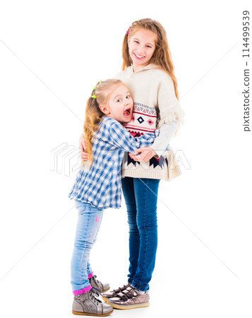 Two little girls sisters in casual clothes posing and hugging each other, isolated on white background Two little girls sisters in casual clothes posing and hugging each other, isolated on white background 114499539