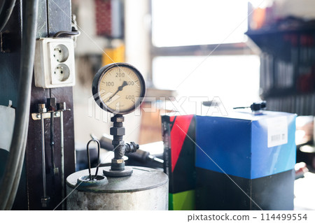 Tire-pressure gauge in auto repair shop. Mechanics repairing, maintaining car in garage, inspecting car tires, wheels. 114499554