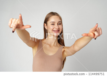 Young Woman Pointing Towards Camera With a Playful Expression in a Studio Young Woman Pointing Towards Camera With a Playful Expression in a Studio 114499751