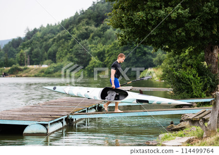 Young canoeist carry canoe and paddle, going into water, walking on wooden dock. Concept of canoeing as dynamic and adventurous sport Young canoeist carry canoe and paddle, going into water, walking on wooden dock. Concept of canoeing as dynamic and adventurous sport 114499764