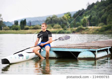 Young canoeist sitting on wooden dock. Concept of canoeing as dynamic and adventurous sport. 114499783