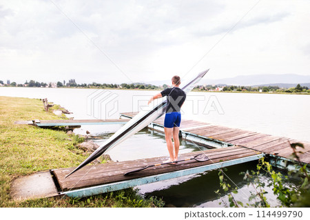 Young canoeist carry canoe and paddle, going into water, walking on wooden dock. Concept of canoeing as dynamic and adventurous sport 114499790